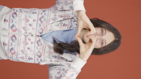 Vertical-video-of-Young-woman-making-heart-sign-at-camera.
